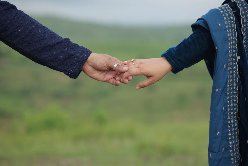 Young Indian couple holding hands, blurred summer landscape in the background - marriage loyalty