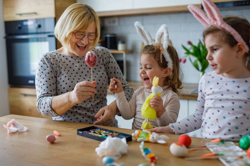 Grandchildren and grandmother painting eggs for Easter holiday in kitchen