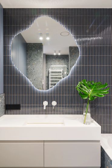 Modern bathroom with unique mirror and dark tiled wall.