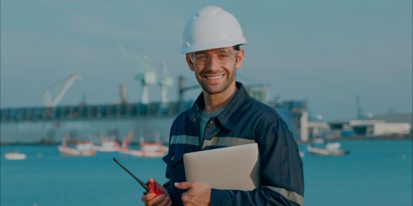 Engenheiro sorridente com capacete e rádio em porto.