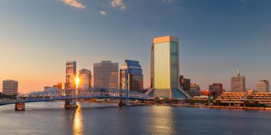 Sunset over a city skyline with buildings reflecting on the water.