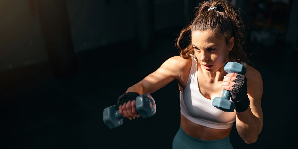 Woman intensely exercising with dumbbells in a gym.