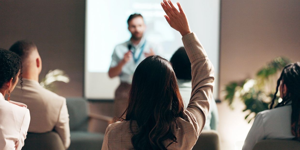 A woman raises her hand during a presentation in a professional setting.