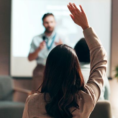 Person raising hand in a classroom or seminar setting.