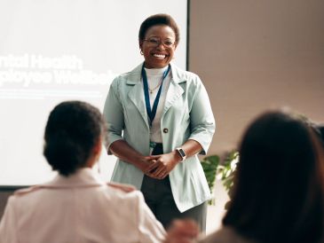 A smiling woman leading a mental health workshop for employees.