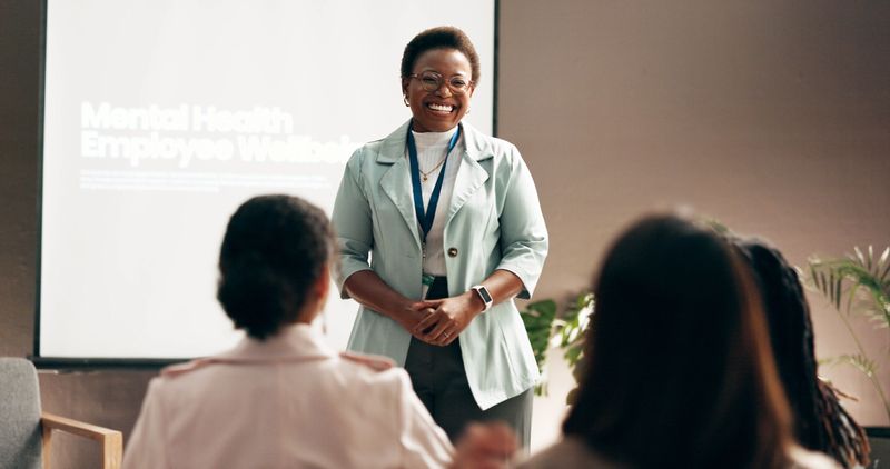 Happy woman, presentation and meeting with group for mental health program or employee wellbeing at office. Female person, speaker or crowd with smile for seminar, conference or social workshop