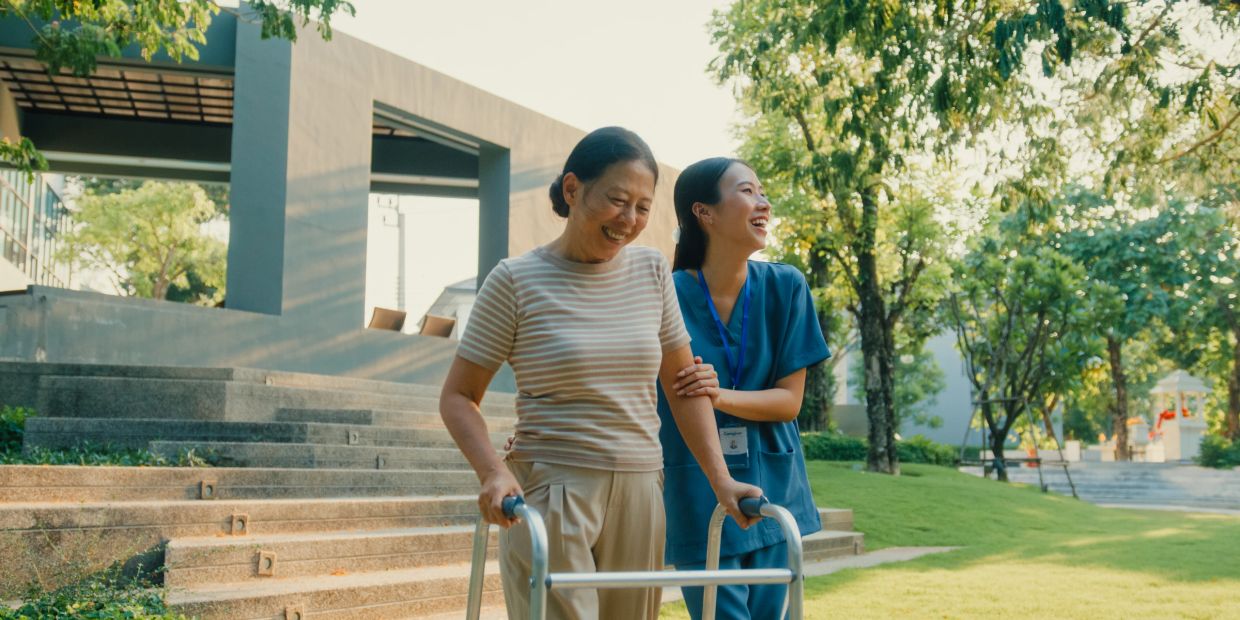 Senior woman walking with a nurse using a walker outside.