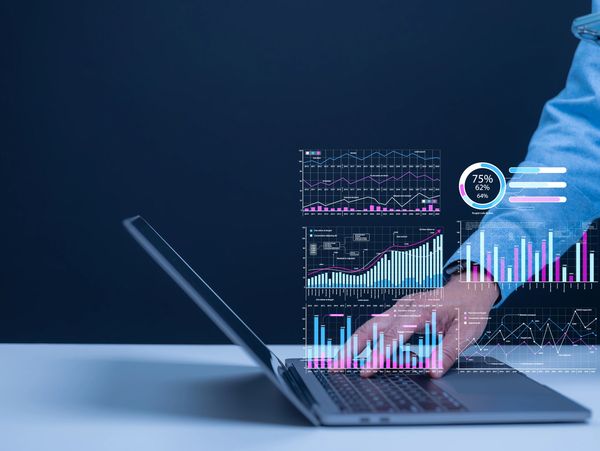 Person analyzing data charts projected from laptop while using a smartphone.