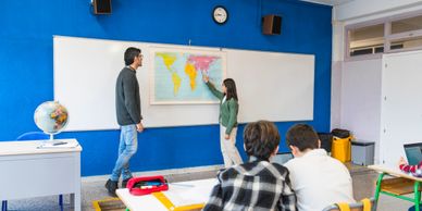 Teacher and student discussing a world map in a classroom.