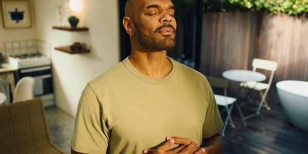 Man meditating indoors with eyes closed and hands on chest.