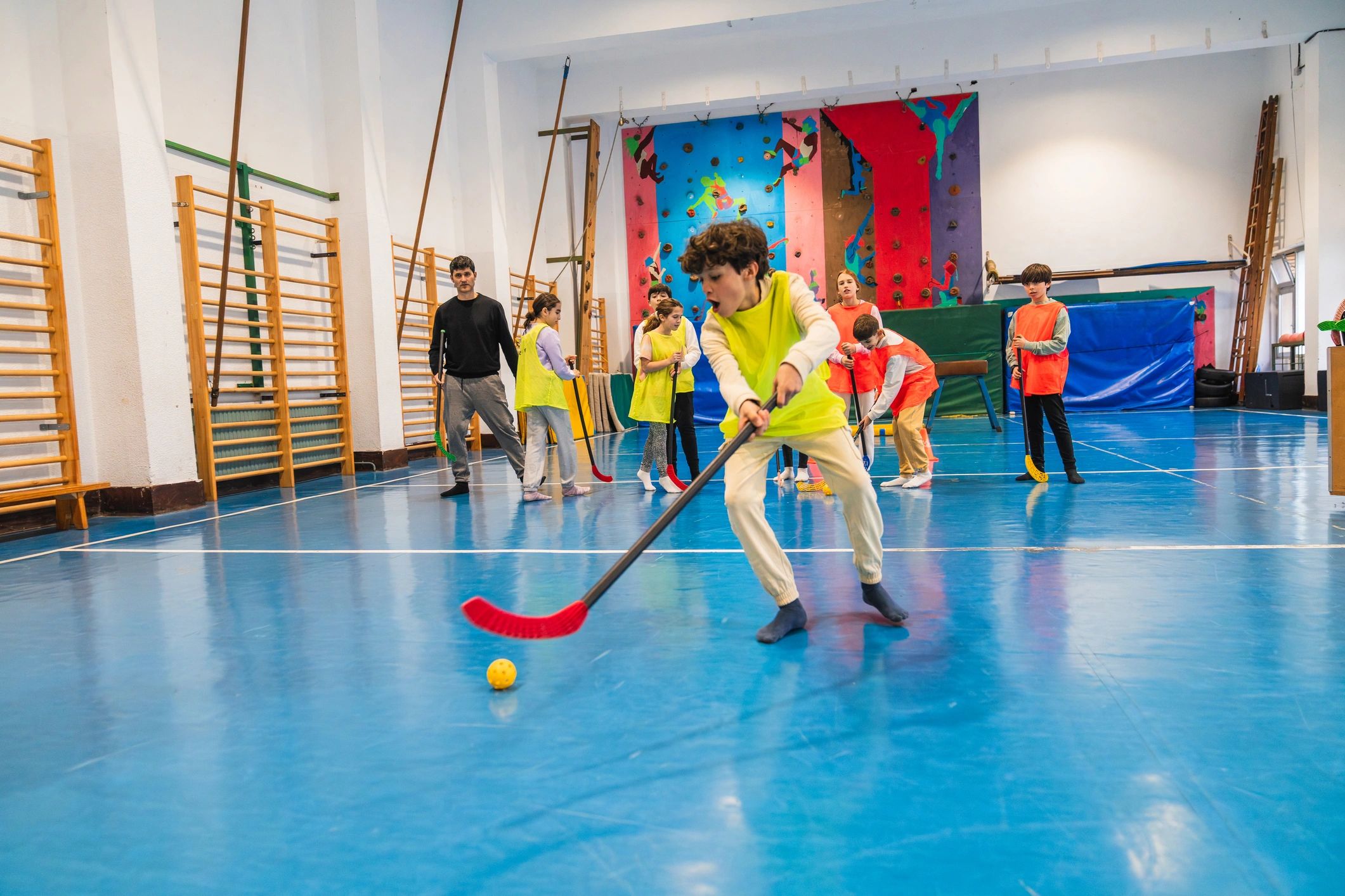 Children playing floor hockey indoors with a coach.