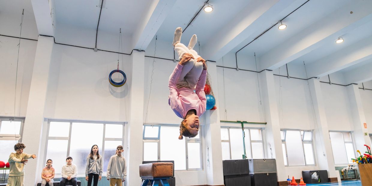 A child performs a mid-air somersault in a gymnasium while others watch.
