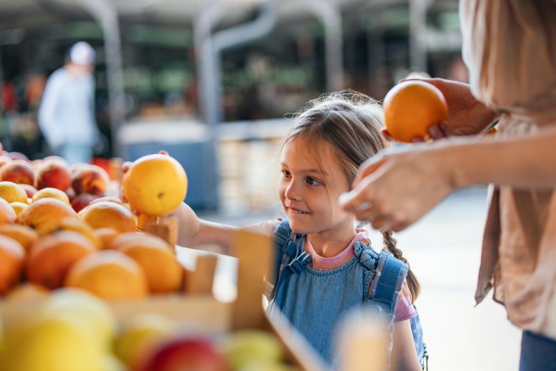 A child enjoys choosing fresh produce at a local farmer's market, surrounded by vibrant fruit stands. This scene portrays a joyful moment representing health, family bonding, and making wholesome food choices.