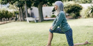 Older woman stretching outdoors on a grassy lawn.