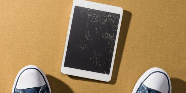 Cracked tablet screen on the floor with shoes nearby.