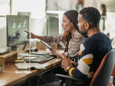 Two colleagues analyzing financial data on a computer screen in an office.