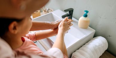 Adult helping child wash hands with soap at a sink.