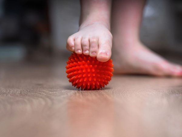 Foot pressing on a red spiky massage ball on wooden floor.