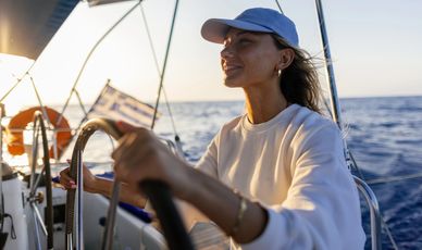 A woman steering a sailboat on a calm sea during sunset.