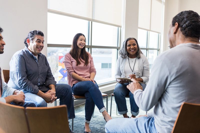 Multiracial group of adults in a therapy session, showing togetherness and emotional support.
