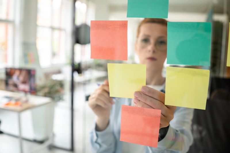 In a modern office setting, a person organizes colorful sticky notes on a transparent surface, showcasing creativity and effective task management. The indoor space is bright and inviting.