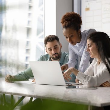 Three colleagues collaborating around a laptop in a bright office.