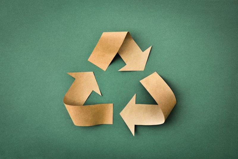 Recycling symbol with arrows made of brown paper on a green textured background. Top view.