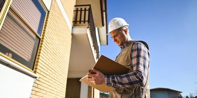 Construction worker inspecting a building with clipboard under clear blue sky.