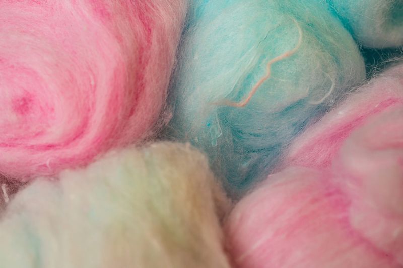 Close-up of fluffy pastel cotton candy in pink, yellow, and peach tones. Sweet treat perfect for dessert and carnival themes.