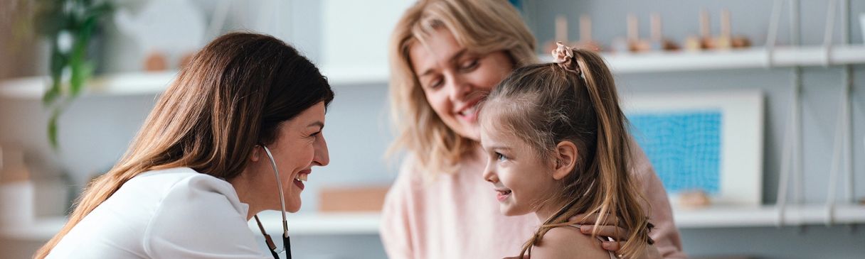 A doctor smiling at a happy little girl with a woman behind her.