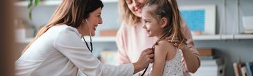 A doctor smiling at a happy little girl with a woman behind her.