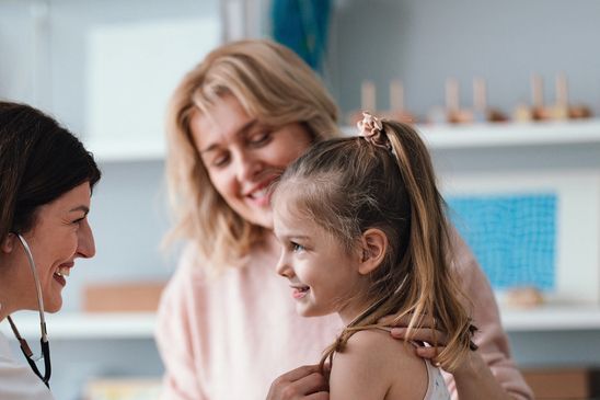 A doctor smiling at a happy little girl with a woman behind her.