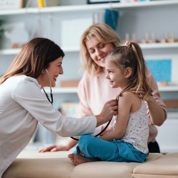 A doctor smiling at a happy little girl with a woman behind her.