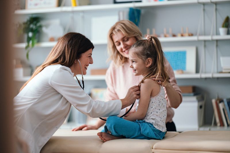 A friendly pediatrician performs a health examination for a happy young girl, observed by her caring mother. The image conveys family care, child health, and professional medical service.