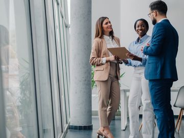 Three colleagues discussing work in a modern office with large windows.
