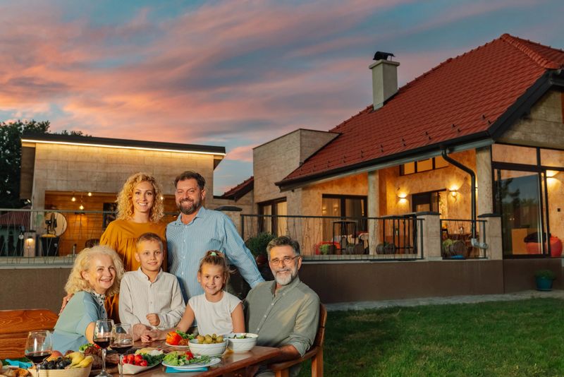 Family enjoying outdoor dinner in backyard of modern house at sunset