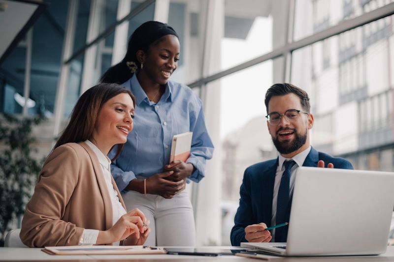 Diverse businesspeople collaborating on a project, using a laptop in a modern office environment
