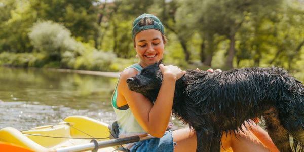 Woman smiles hugging her wet dog on a kayak in a river.