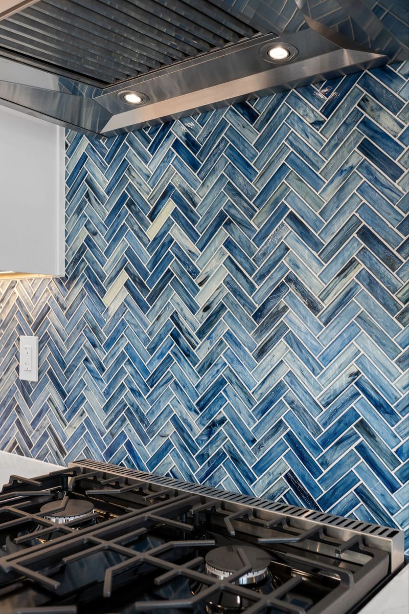 Contemporary kitchen with white cabinetry, patterned tile floor, blue backsplash, and stainless steel appliances.