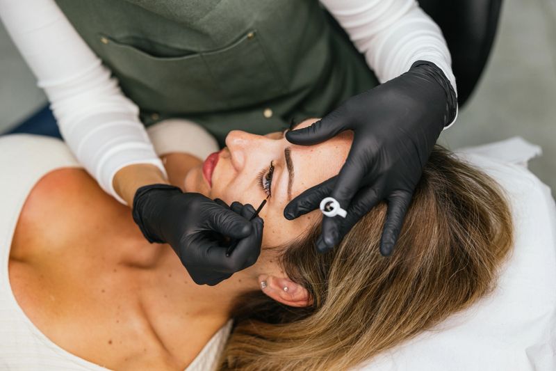 Beautician wearing black gloves applying permanent eyeliner makeup on a young woman's eyelid