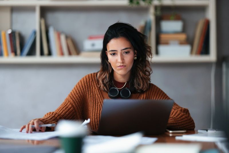 A dedicated student engaged in studies, working attentively on her laptop in a cozy and quiet library environment, surrounded by books and soft lighting.