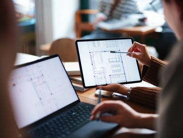 Two people reviewing architectural floor plans on a tablet and laptop.