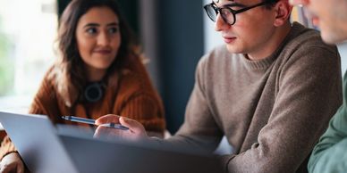 Three young adults collaborating over laptops in a cozy workspace.