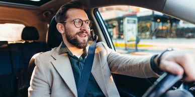 Smiling man wearing glasses driving a car on a sunny day.