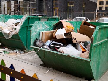 Two large green dumpsters filled with construction and packaging waste.