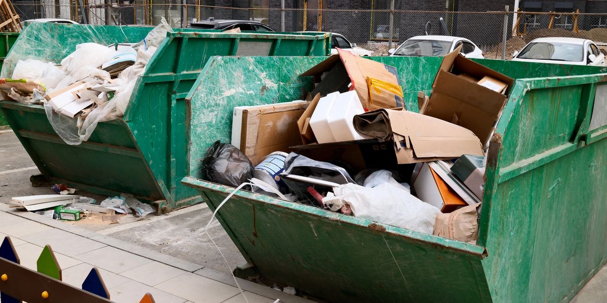 Two large green dumpsters filled with construction debris and cardboard boxes.