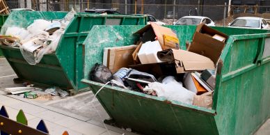 Two green dumpsters filled with trash and cardboard boxes.