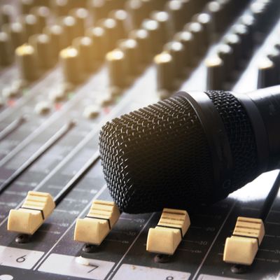 Microphone resting on an audio mixing console's sliders.