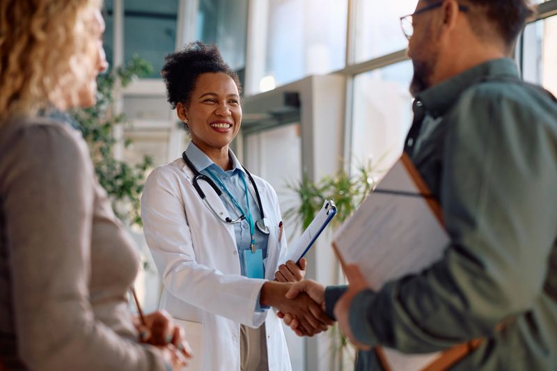 Happy African American doctor greeting a man who came with his wife for medical appointment at the clinic.