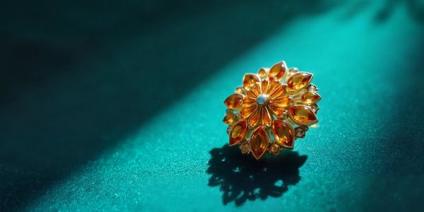Golden flower-shaped brooch with amber stones on teal surface.
